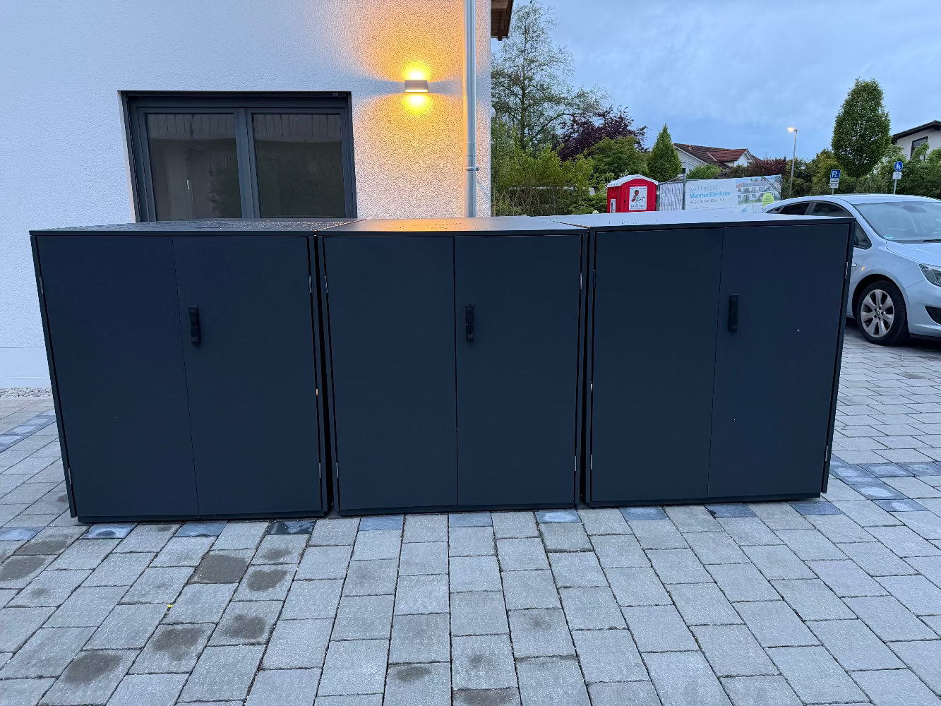 Abgeschlossenes Aufbau-Projekt einer dreiteiligen Metall-Fahrradgarage Statement in Anthrazit auf Pflastersteinen vor einem Wohngebäude.