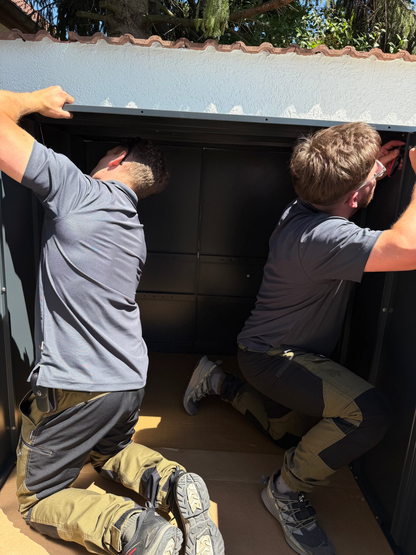 Professioneller Montage-Service für Metallwaren in Deutschland: Zwei Handwerker montieren eine anthrazitfarbene Metall-Gerätebox im Außenbereich.