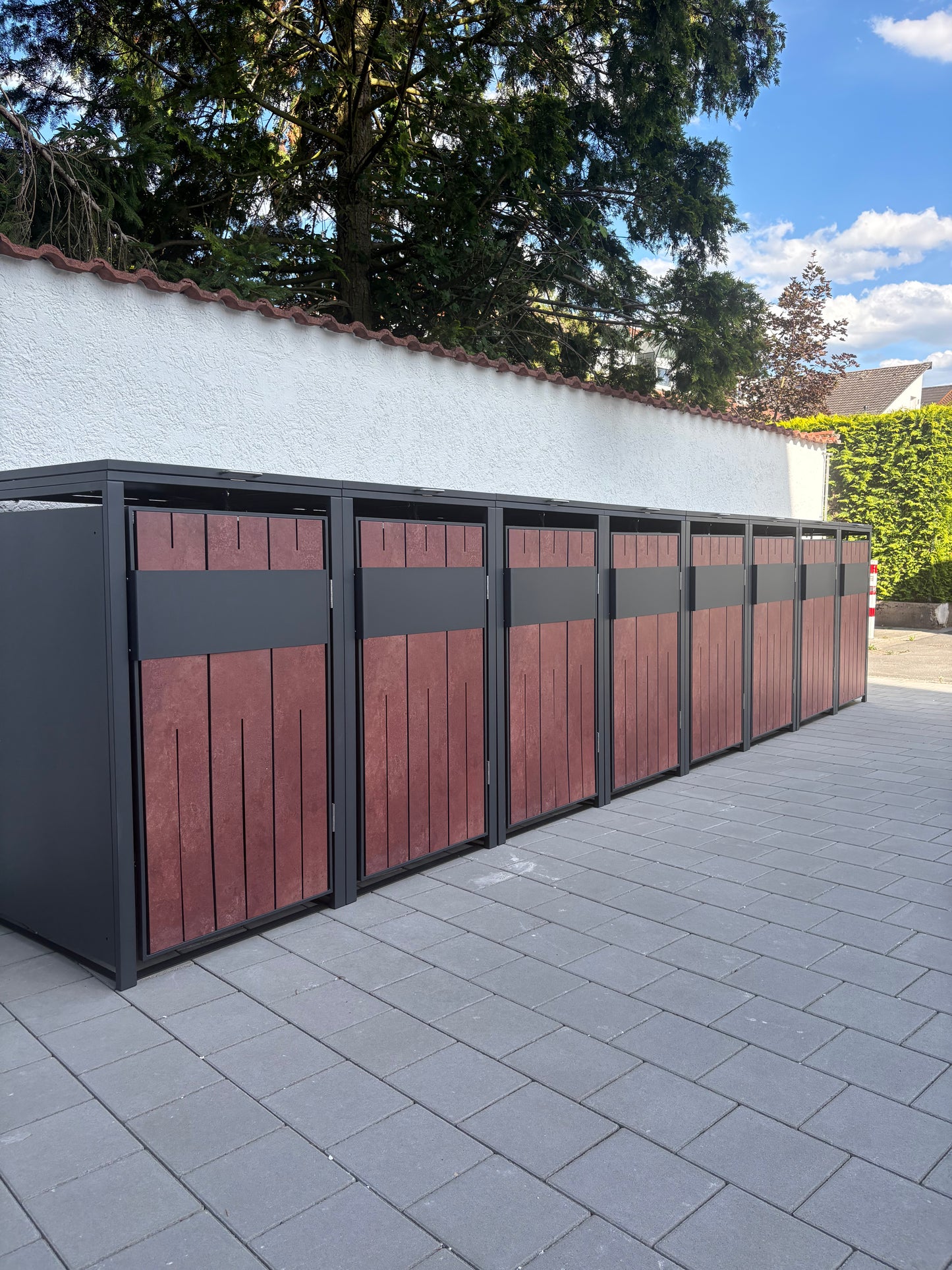 Großes Aufbau-Projekt einer mehrteiligen Mülltonnenbox in Anthrazit mit charakteristischen Fronten aus rötlich-braunem Cortenstahl auf Pflastersteinen.