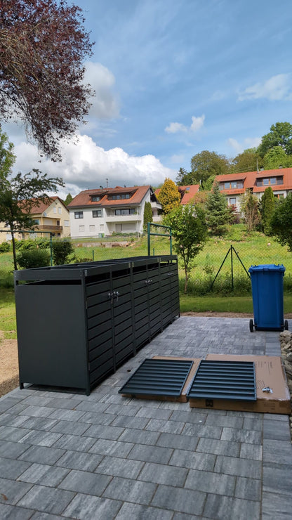Aufbau-Projekt einer anthrazitfarbenen Mülltonnenbox Basic auf einer gepflasterten Terrasse im Garten, während der Montage.