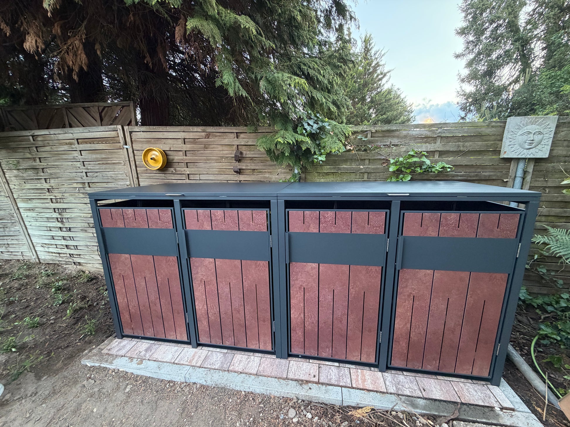 Moderne_Muelltonnenbox_4er_aus_Anthrazit_Metall_mit_Holzoptik_Fronten_und_aufklappbarem_Deckel_im_Aussenbereich